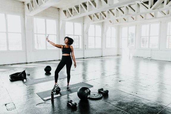 Woman in workout attire stretching in a bright, spacious gym with weights nearby.