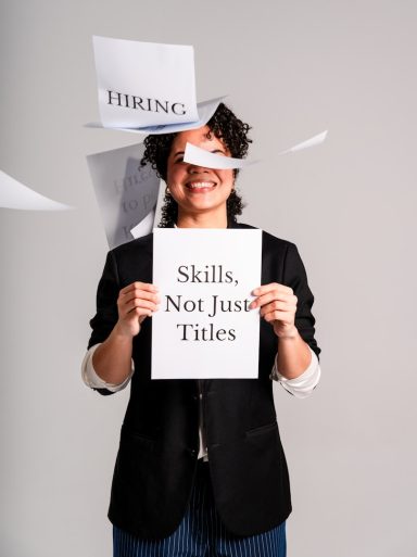 Person holding a sign saying "Skills, Not Just Titles" with papers flying around.