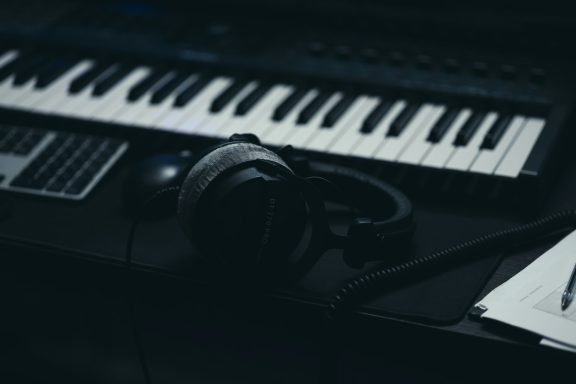 A close-up of a piano keyboard, headphones, and sheets of music on a desk.